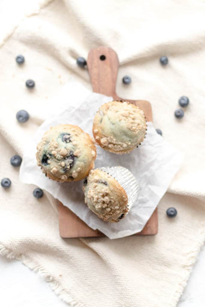 blueberry muffins on parchment paper with blueberries scattered