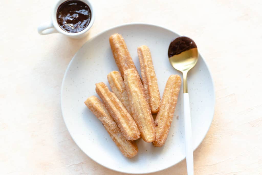 churros on a round plate with a chocolate dipped spoon