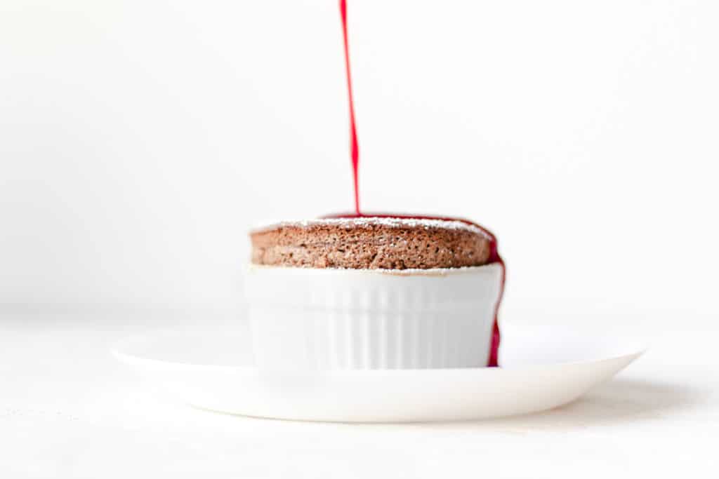 chocolate soufflé with raspberry sauce being drizzled on top 