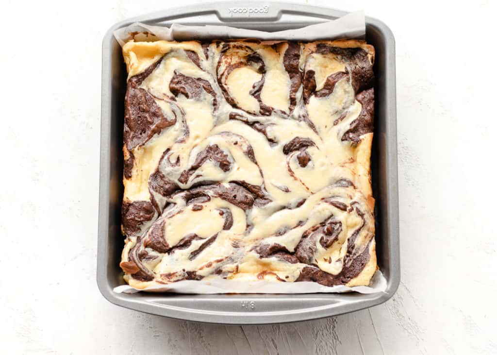 cream cheese brownie in a baking pan lined with parchment paper
