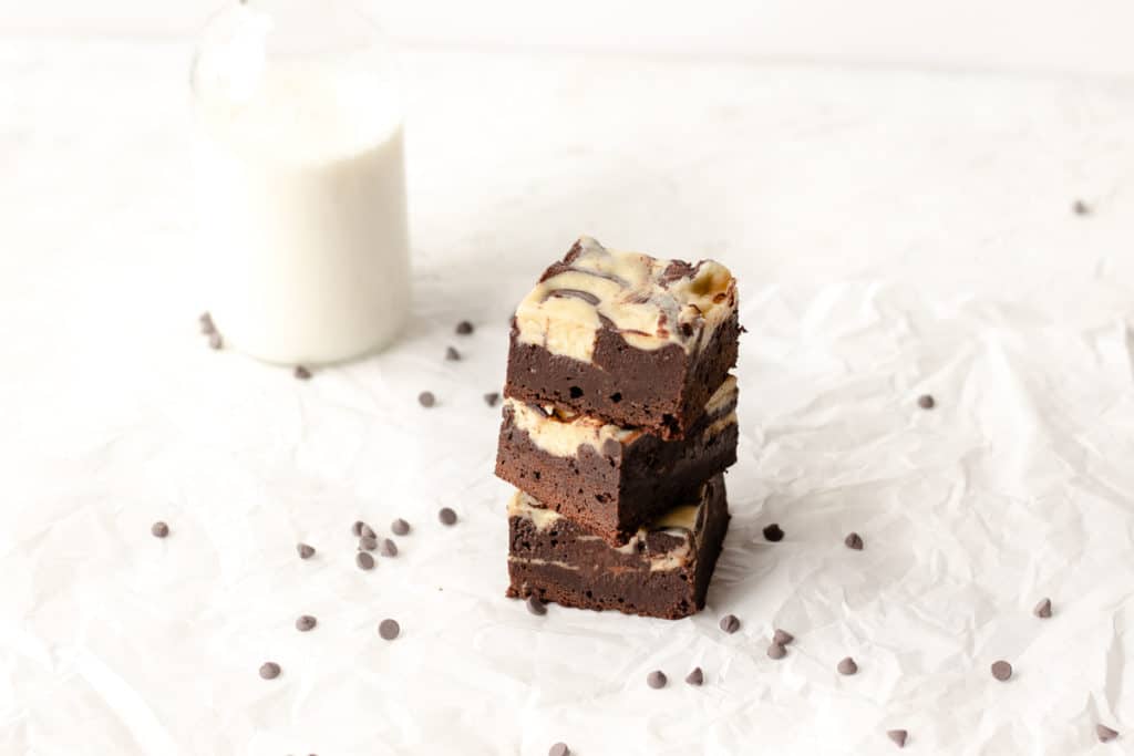 brownies with cream cheese stacked on top of each other with glass of milk