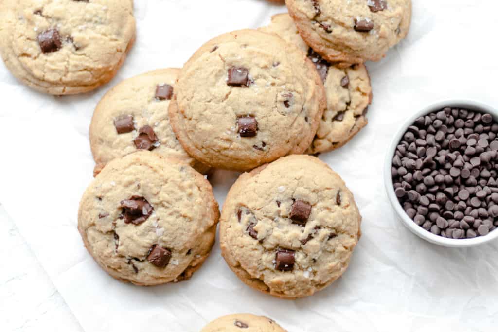 tahini cookies on parchment paper with a bowl of chocolate chips beside it