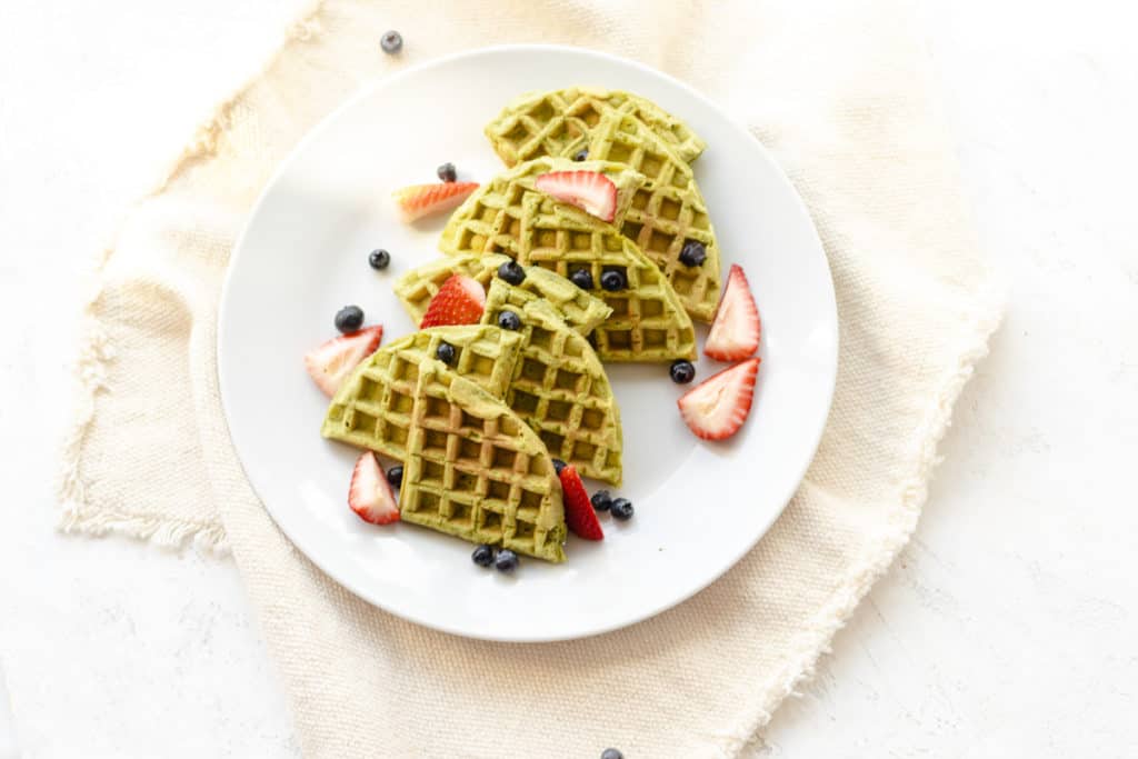 waffles layed on top of each other on a plate with blueberries and strawberries