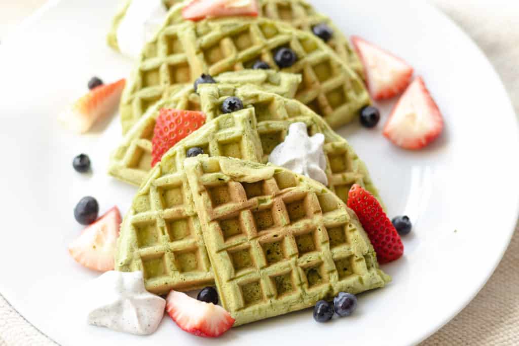 Close-up shot of a stack of matcha waffles topped with fresh strawberries and whipped cream