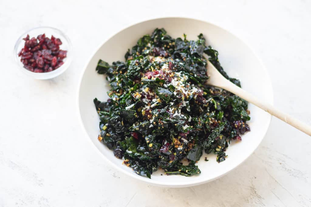 tender kale salad in a bowl with a wooden spoon