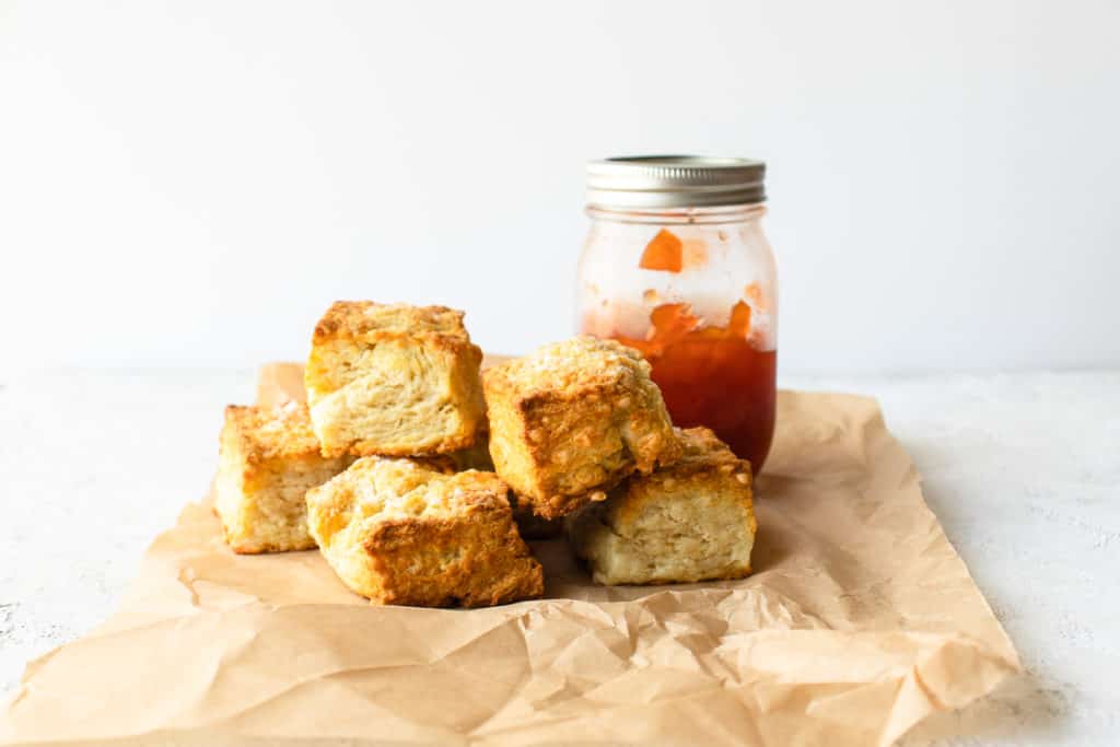 buttermilk biscuits on a sheet of parchment paper with a mason jar of jam on the side
