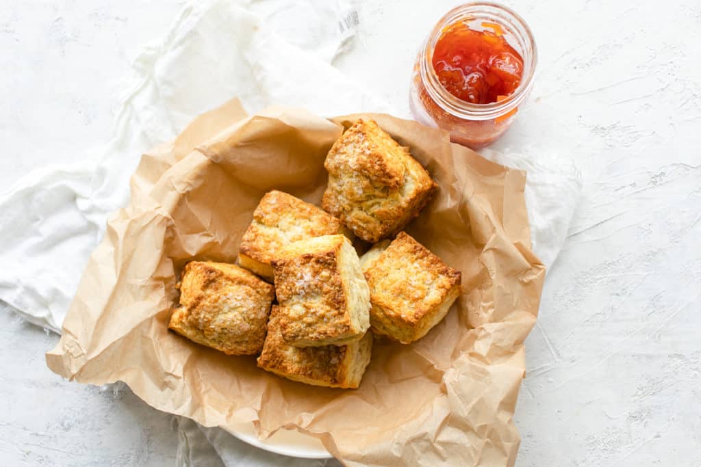flaky biscuits in a bowl with parchment paper and a side of jam 