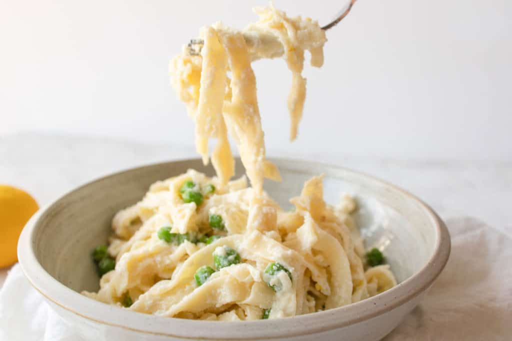 creamy pasta with ricotta, lemon, and peas being lifted up with a fork