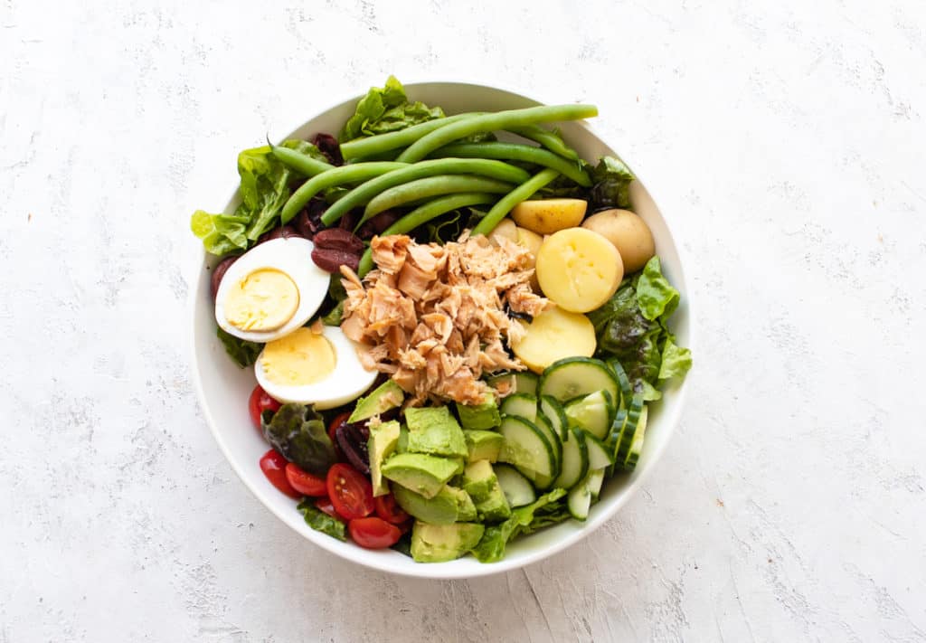 nicoise salad in a bowl with green beans, potatoes, eggs, tomatoes, avocado and tuna