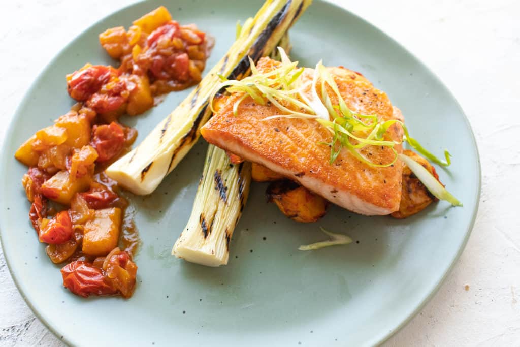salmon garnished with green onions on a plate with charred leeks and sauce
