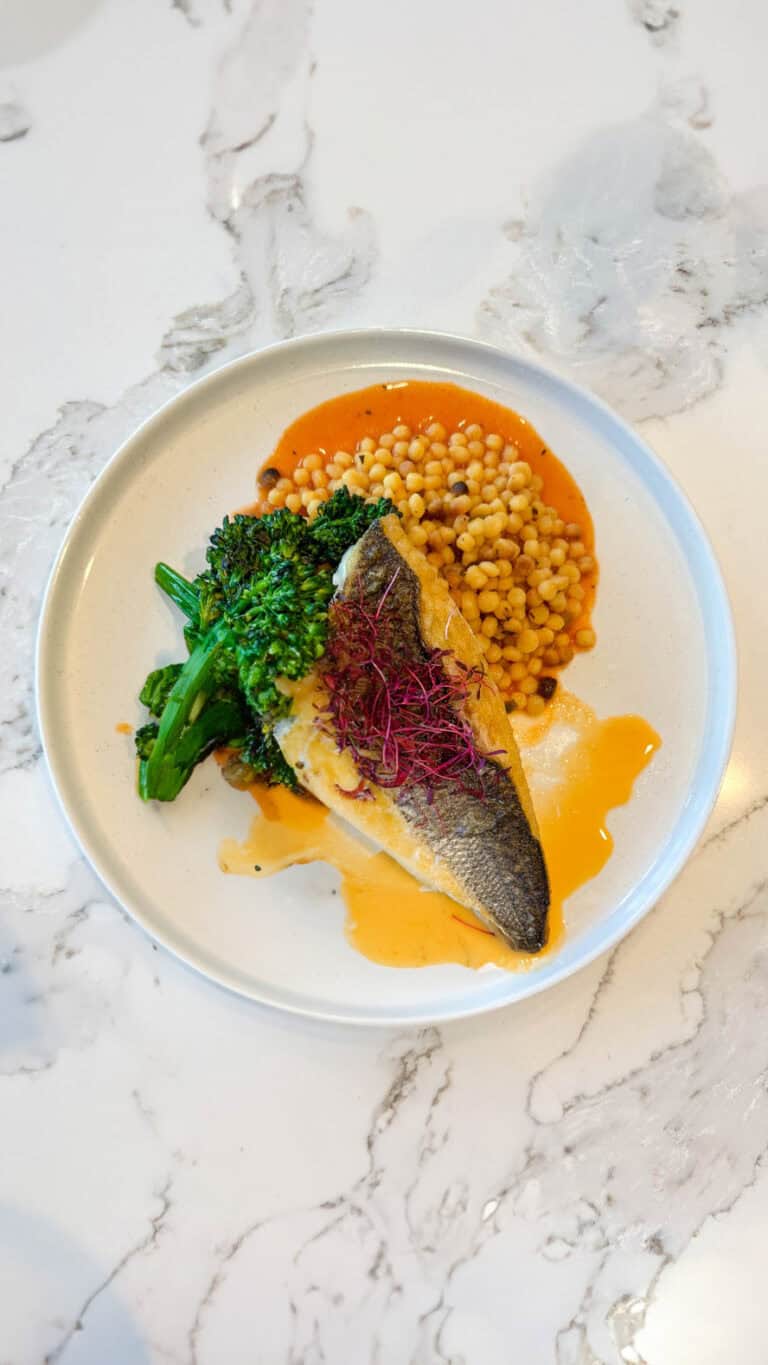 Pan-seared sea bass with broccolini and saffron couscous, plated in a client kitchen