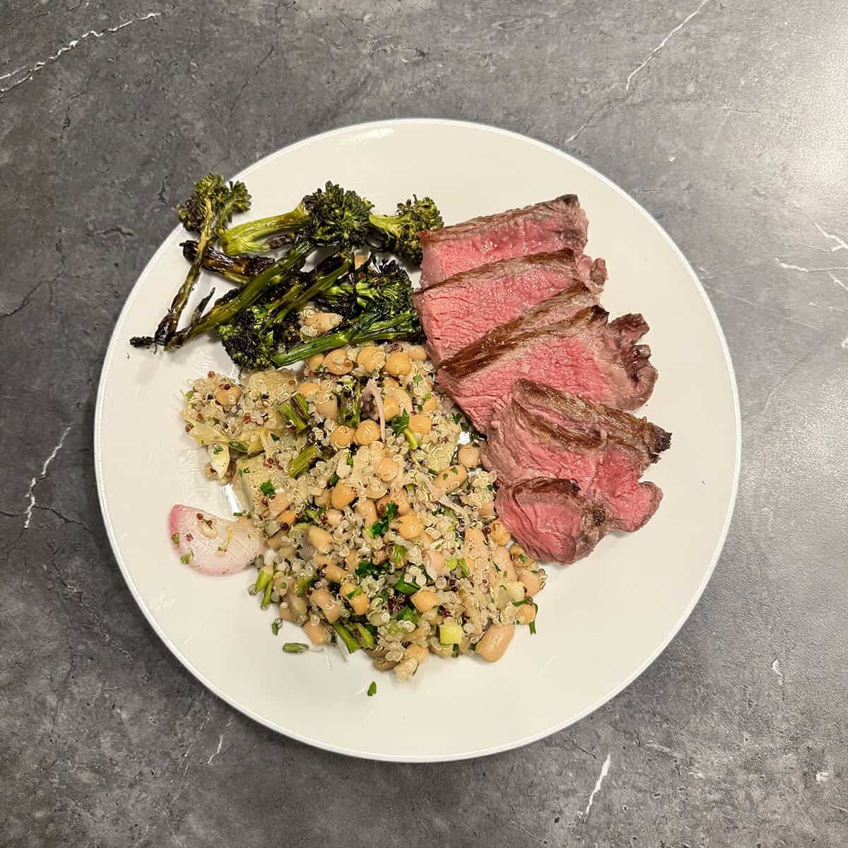 Sliced NY strip steak with charred broccolini and white bean quinoa salad, plated at home