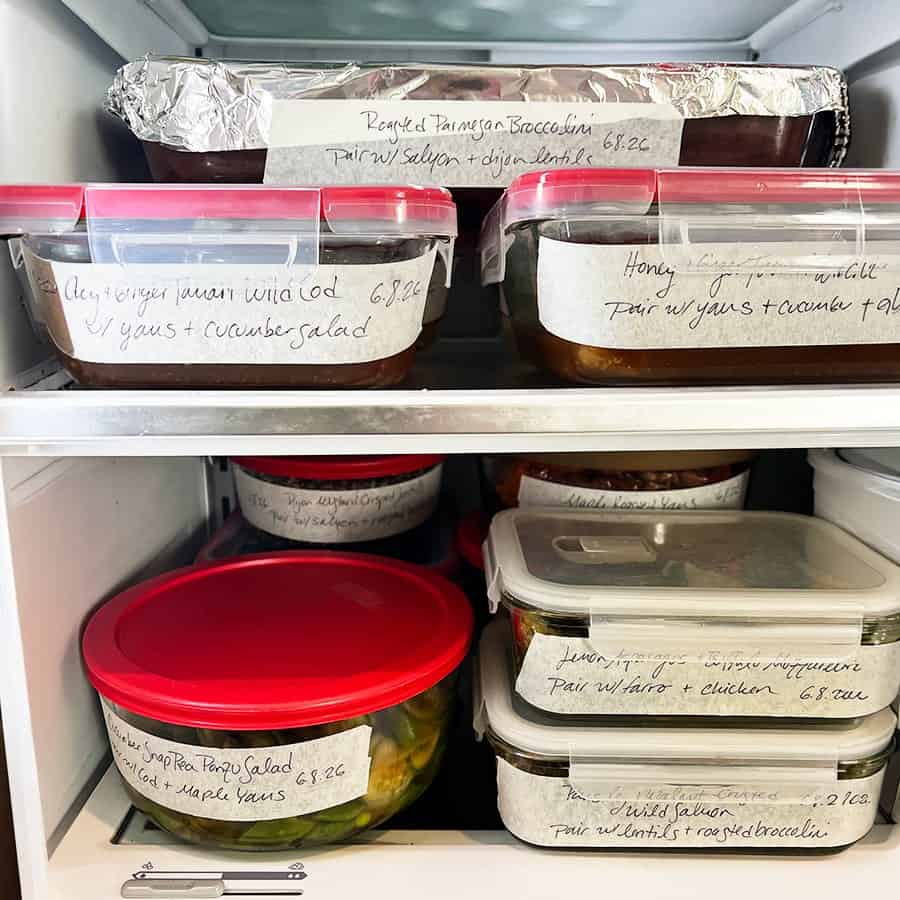 Labeled glass containers of chef-prepared meals stacked in a client’s refrigerator, each with pairing instructions