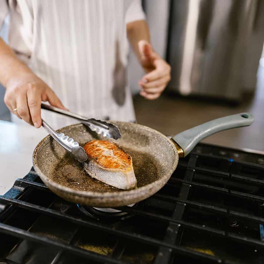 A chef searing salmon in a pan on the client’s stove