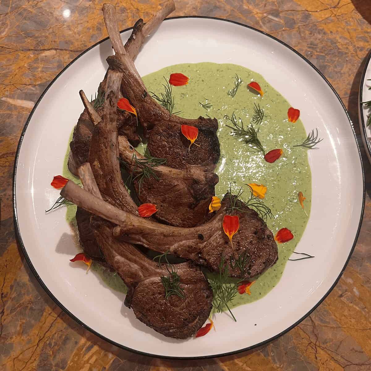 Lamb chops plated over green herb sauce with edible flowers at a private dinner