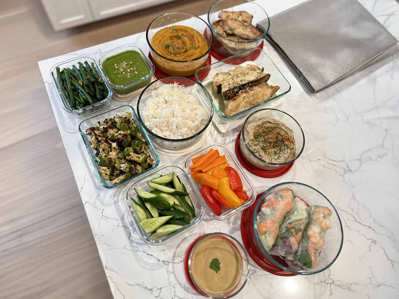 A full week of chef-prepared meals across a client kitchen island — proteins, sides, sauces and fresh vegetables in glass containers