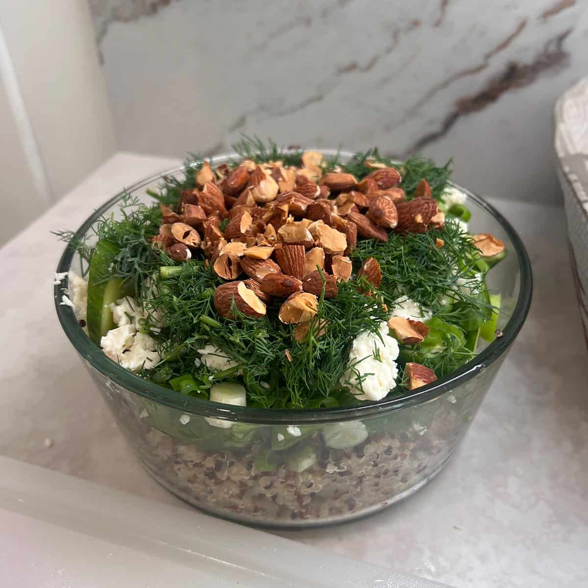 A layered quinoa salad with herbs, feta and almonds in a glass serving bowl