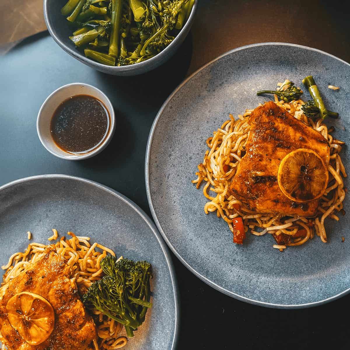 A finished dinner of glazed salmon over noodles with broccolini, plated and ready at home