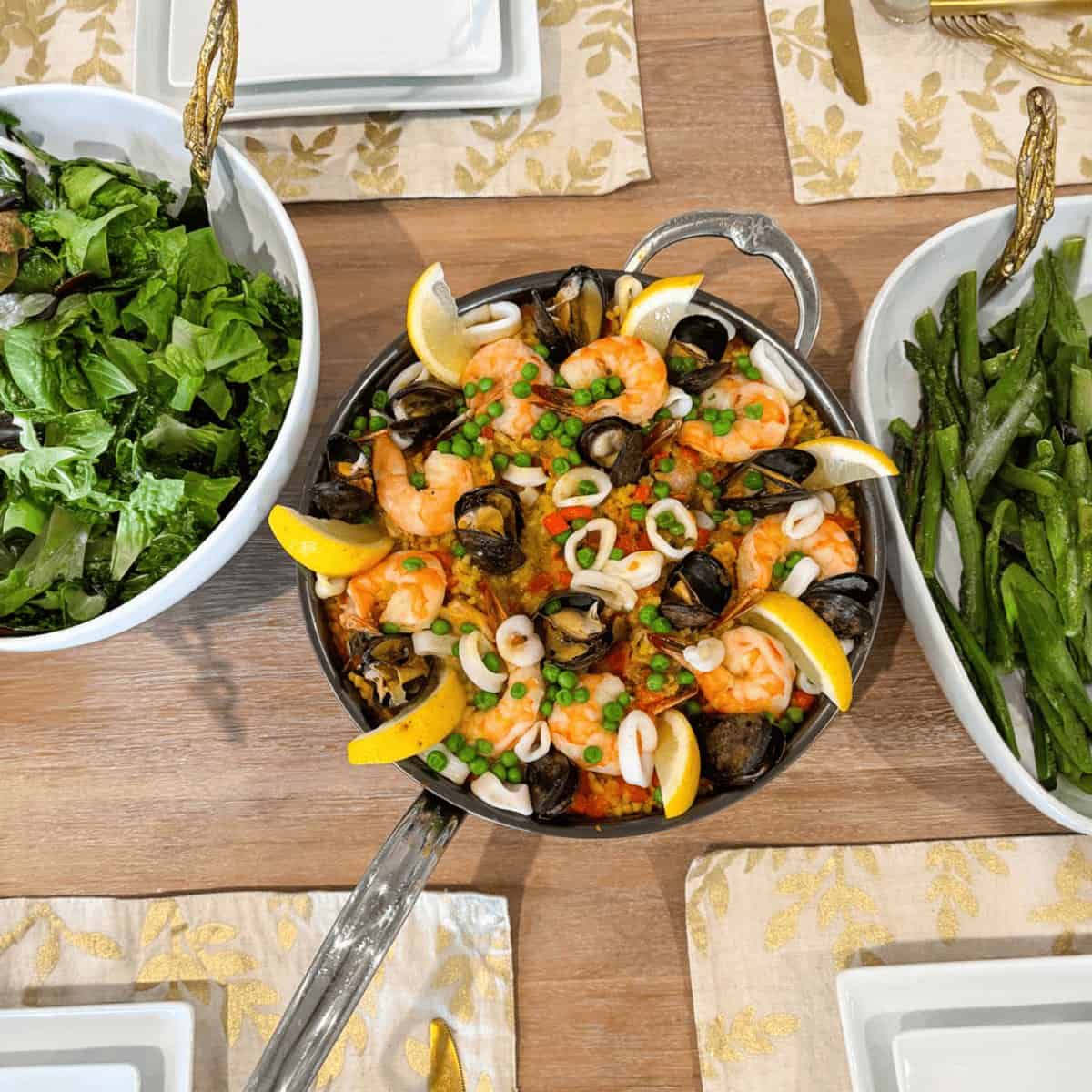 A seafood paella served family-style at a set home dinner table with salad and asparagus
