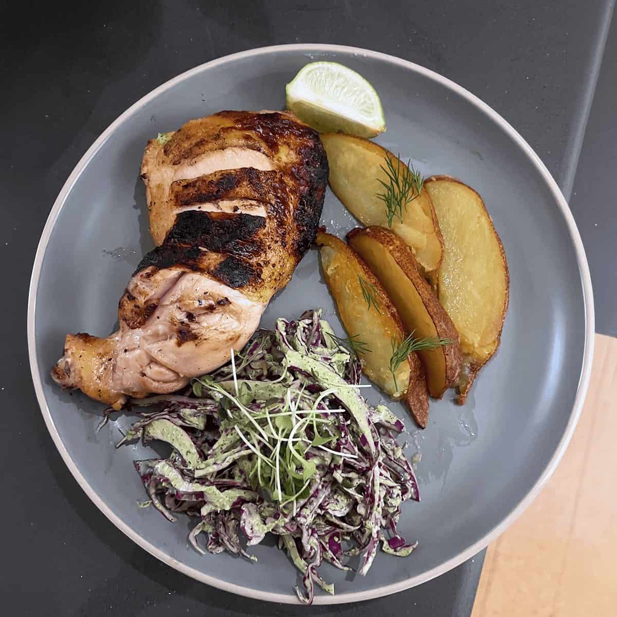 Grilled chicken with roasted potato wedges and herbed slaw on a gray plate