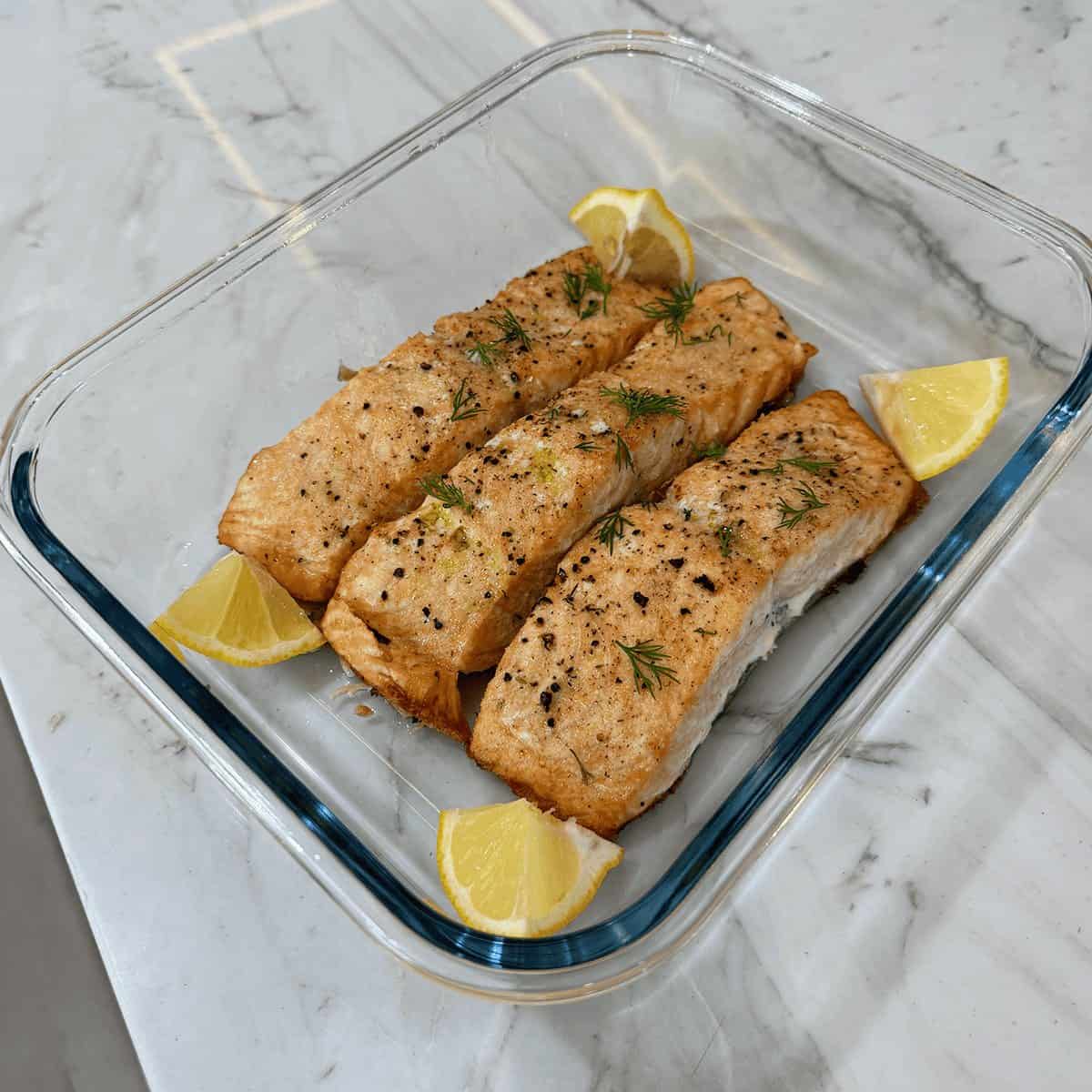 Three herb-roasted salmon fillets with lemon and dill in a glass dish