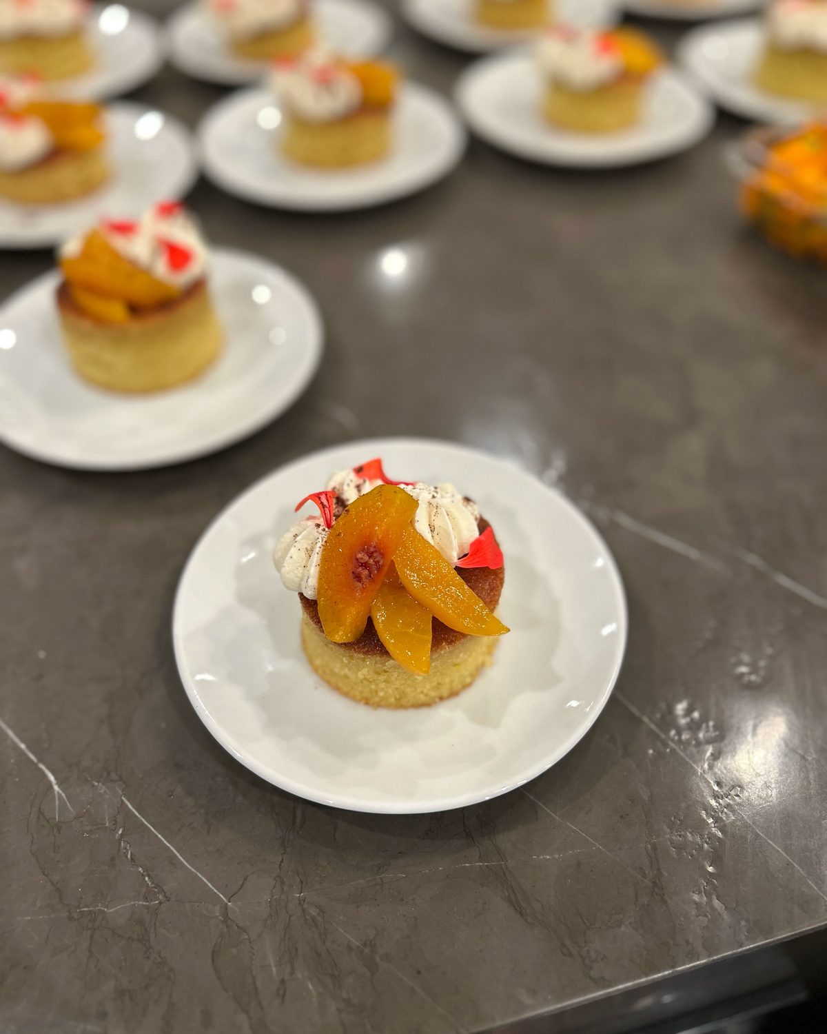 Plated cakes topped with poached peaches lined up for dessert service