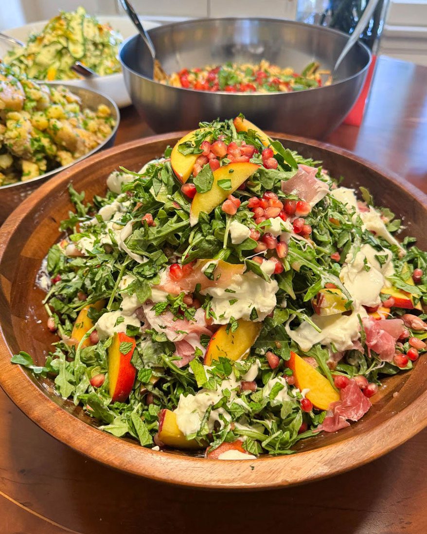 Family-style salad with peaches, pomegranate and prosciutto served with shared dishes at an Eats by Nicole dinner party