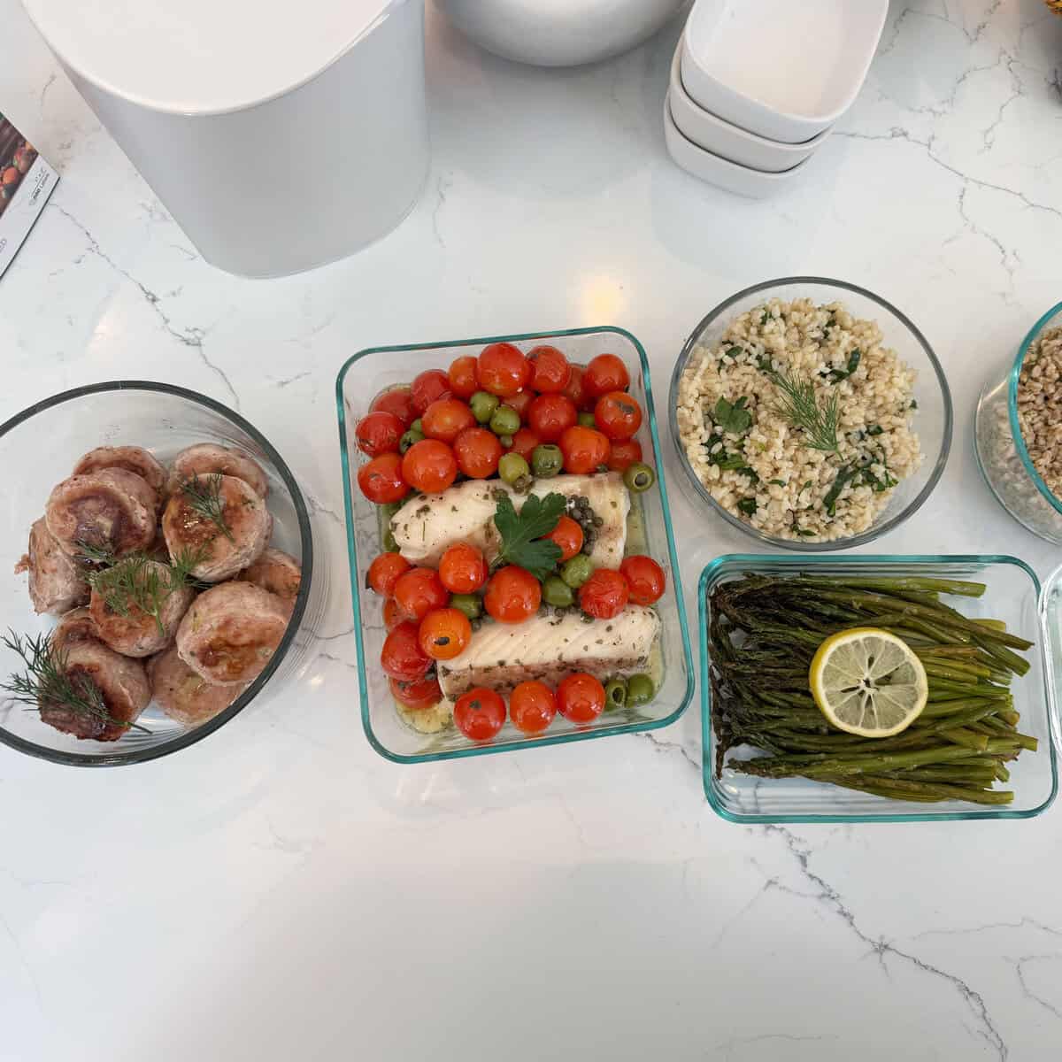 Roasted fish with tomatoes and olives, asparagus with lemon, and herbed grains in glass containers