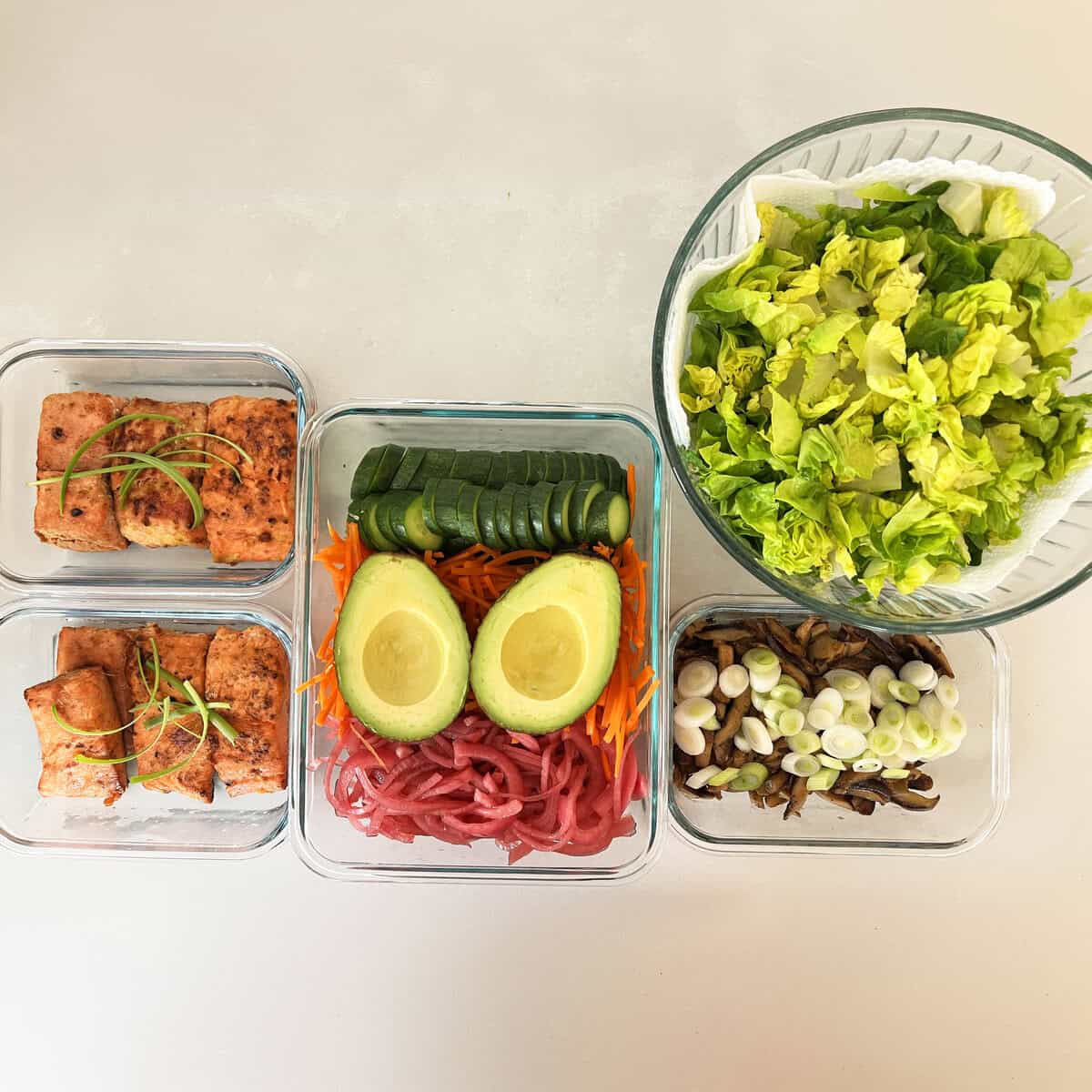 Seared salmon with cucumber, avocado, carrot and pickled onion portioned in glass containers